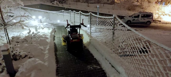 Clearing snow from a path outside a building with a small machine before dawn